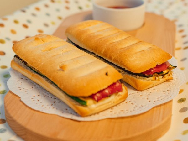 Two panini on wooden board with a cup of tea or coffee alongside. Image by Bert Christaens on Pexels.com